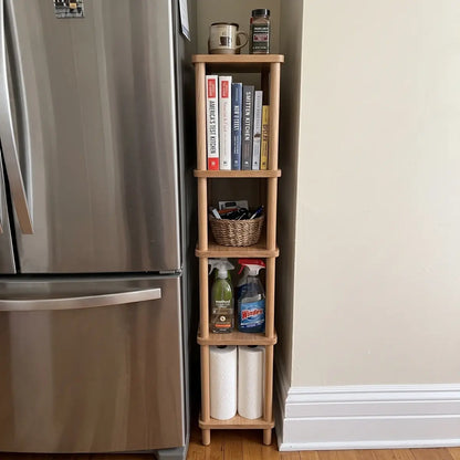 Narrow red oak storage shelf beside a refrigerator with books, baskets and household items