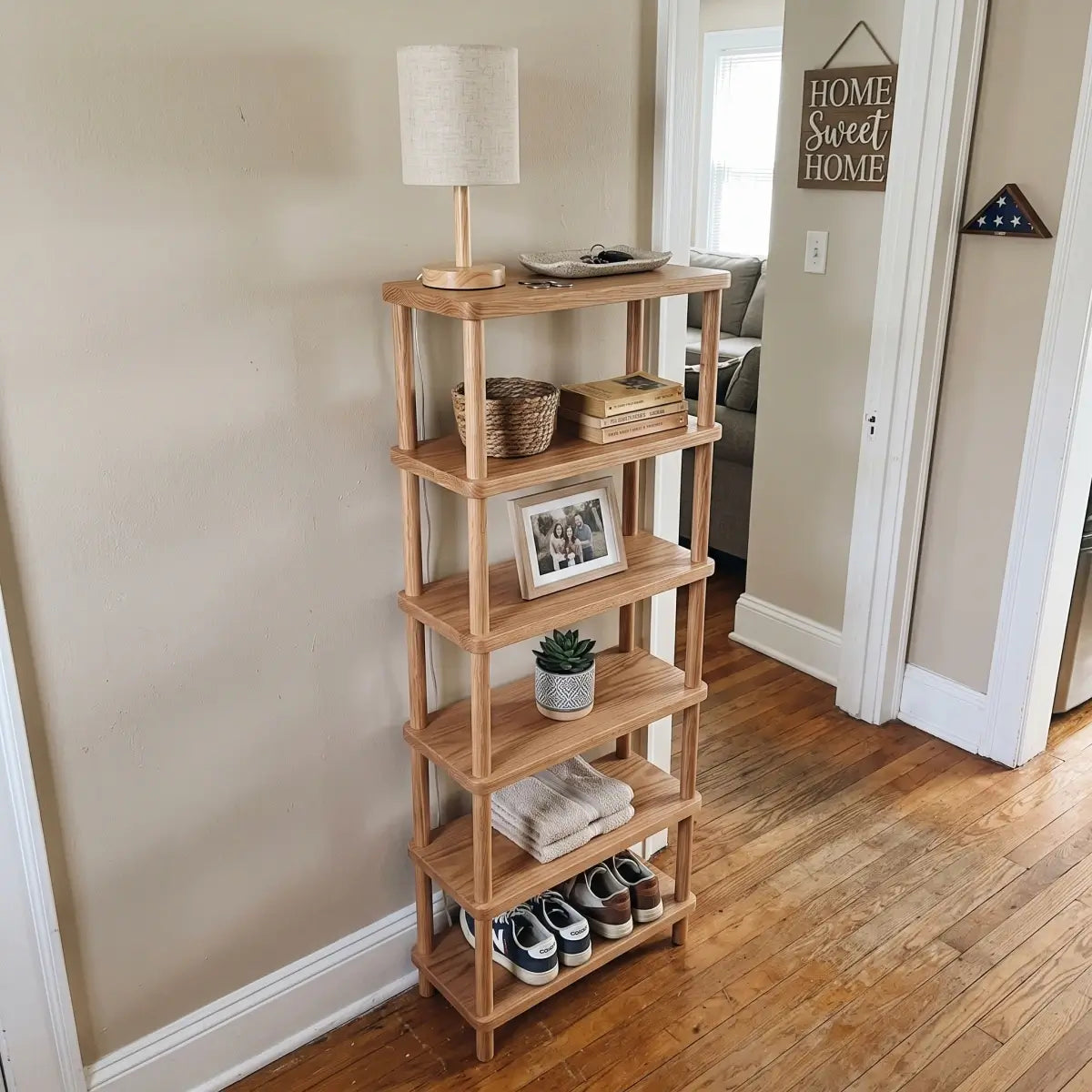 Tall open red oak storage shelf with books, decor, baskets and shoes in a compact room